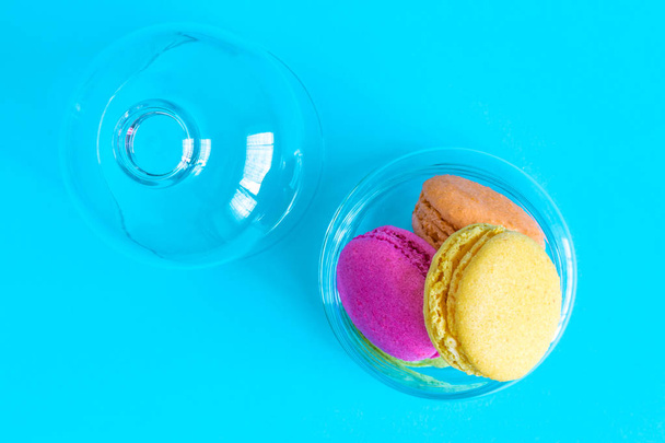 High angle view of multicolored macaroons in bowl isolated on blue. - Фото, изображение
