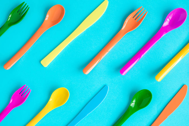 Multicolored plastic spoons, forks and knives pattern isolated on blue. - Фото, зображення