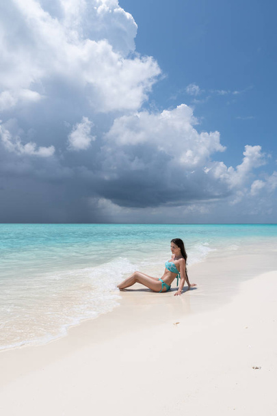 ターコイズの水着を着た若い女の子が白いビーチに横たわっている. - 写真・画像