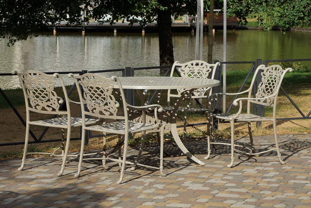 tavolo bianco e sedie in piedi sulla strada sul marciapiede in un parco sul lago
 - Foto, immagini