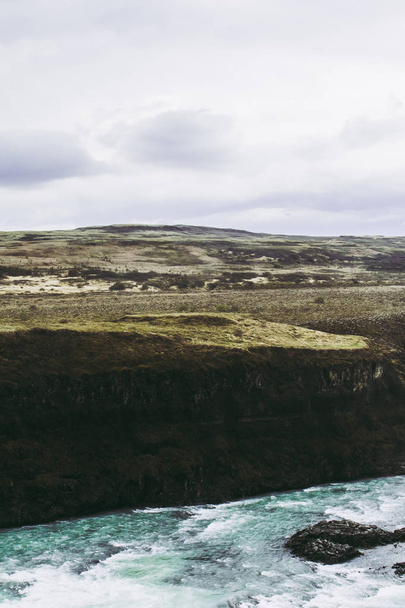 Türkisfarbenes Wasser des Hvita-Flusses, schwarze Felsen und blassgrünes Gras. die Schönheit isländischer Landschaften - Foto, Bild