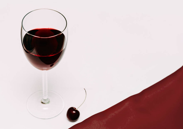 A glass of cherry wine on a red and white background and cherry berries. - Zdjęcie, obraz
