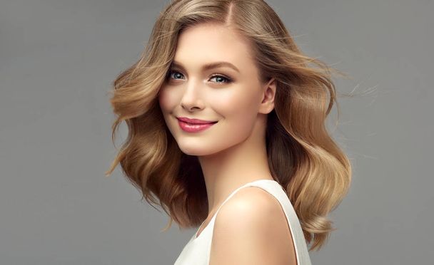 Blonde woman with curly beautiful hair on gray background. The girl with a pleasant smile. Short haircut . Bob hairstyle - Photo, Image