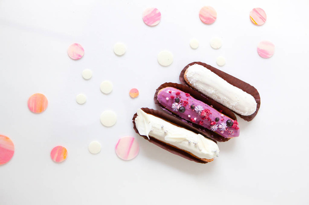 A set of three eclairs with different fillings and design isolate on a white surface decorated with drops of white chocolate - Foto, Imagen