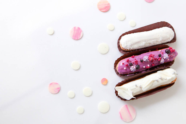 A set of three eclairs with different fillings and design isolate on a white surface decorated with drops of white chocolate - Fotoğraf, Görsel