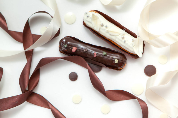 Közeli fel egy sor két eclairs különböző töltelékek és design izolátum fehér felületen díszített csokoládé csepp, fehér és barna selyem szalag - Fotó, kép