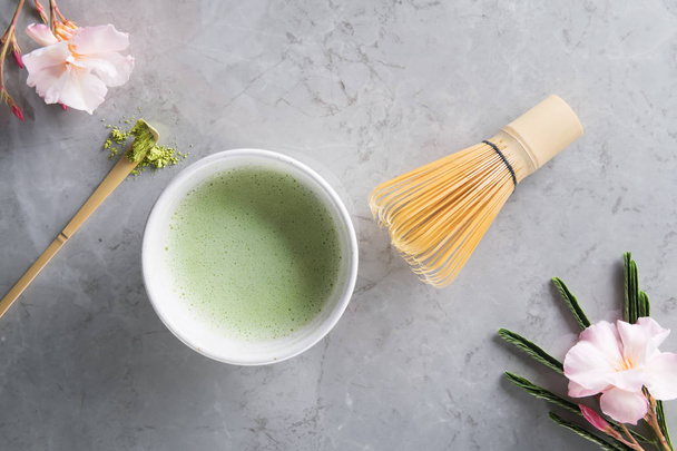 Ansicht von grünem Tee Matcha in einer Schüssel auf grauer Marmoroberfläche mit schöner Oleanderblüte - Foto, Bild