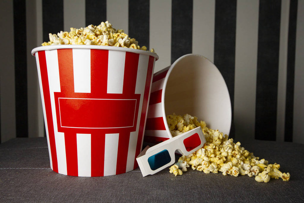 two cardboard buckets of popcorn stand on a gray background with glasses, on the packs there is an copy space for text - Photo, image