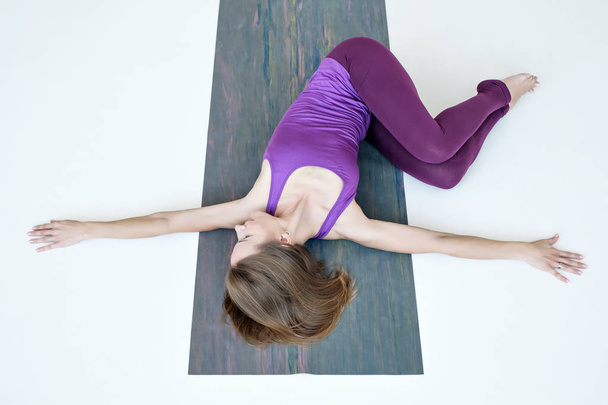 vrouw doet yoga oefening op vloer variatie van buik twist pose - Foto, afbeelding