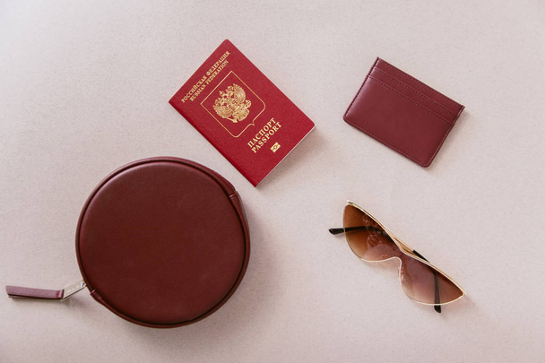 Female minimum travel set. Maroon passport, cardholder and wallet with a bag and glasses on a pastel beige background. - Fotoğraf, Görsel