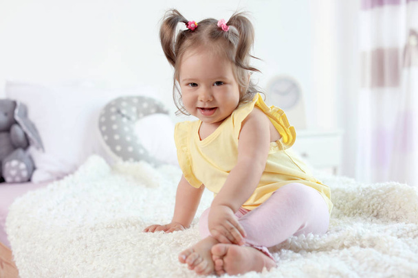 Чарівна маленька дівчинка сидить на ліжку в кімнаті
 - Фото, зображення