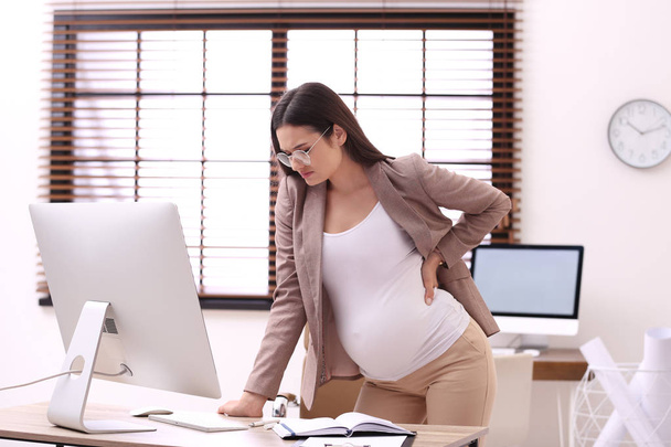 Young pregnant woman suffering from pain while working in office - Foto, Imagem