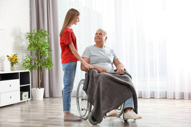 Teenage girl with grandfather in wheelchair at home - Фото, зображення