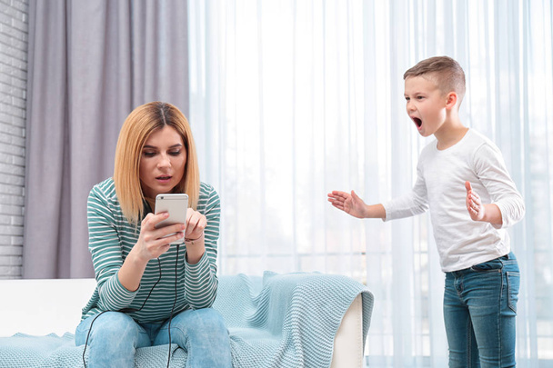 Mother using mobile phone while her son screaming and asking for attention at home. Lonely despaired child - Fotoğraf, Görsel