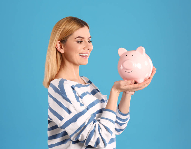 Woman with piggy bank on color background - Foto, afbeelding