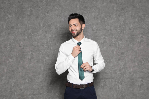 Portrait of businessman straightening tie on grey background - Foto, Imagen