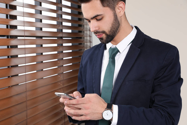 Portrait of businessman with mobile phone at window indoors, closeup. Space for text - Photo, image