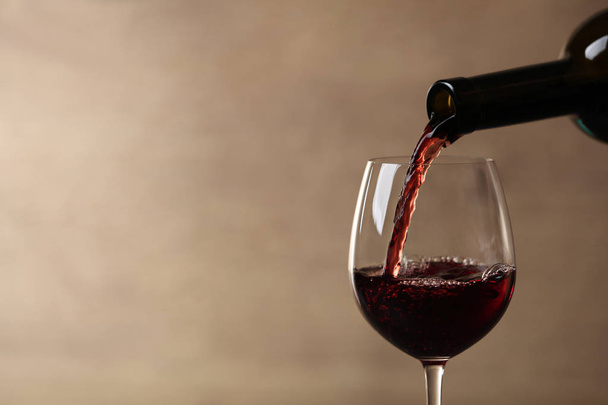 Pouring red wine into glass from bottle against blurred beige background, closeup. Space for text - Photo, image