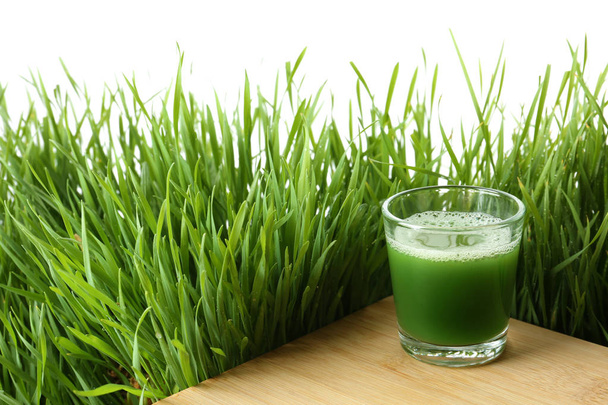 Glass of juice on table and fresh wheat grass against white background. Space for text - Φωτογραφία, εικόνα
