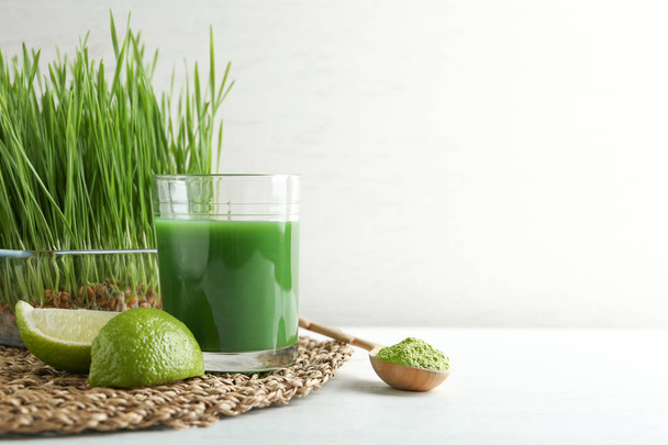 Composition with glass of wheat grass juice and lime on table against light background. Space for text - Photo, Image