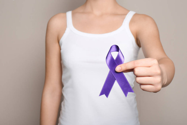 Vrouw met paarse lint op grijze achtergrond, close-up. Huiselijk geweld bewustzijn - Foto, afbeelding