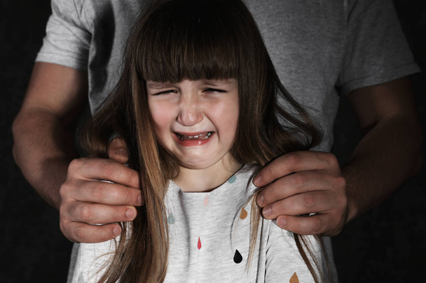 Crying little girl and adult man on dark background, closeup. Child in danger - 写真・画像