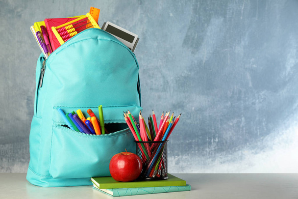 Bright backpack with school stationery on table against blue background, space for text - Foto, afbeelding