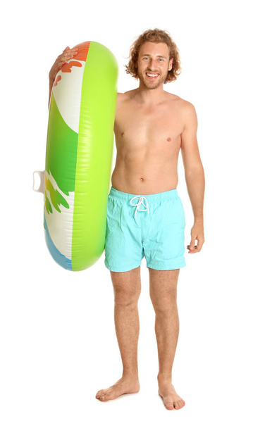 Attractive young man in swimwear with colorful inflatable ring on white background - 写真・画像