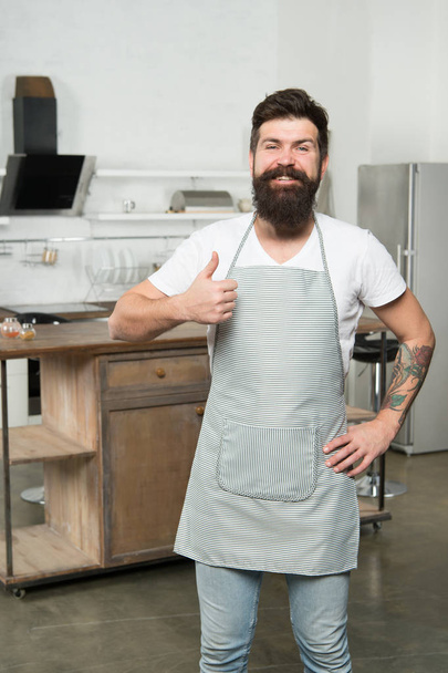 Thumbs up because I like kitchen life. Kitchen inspiration. Attractive kitchen manager. Bearded man smiling and gesturing thumbs up in kitchen. Happy cook wearing apron on show kitchen in restaurant - Fotografie, Obrázek