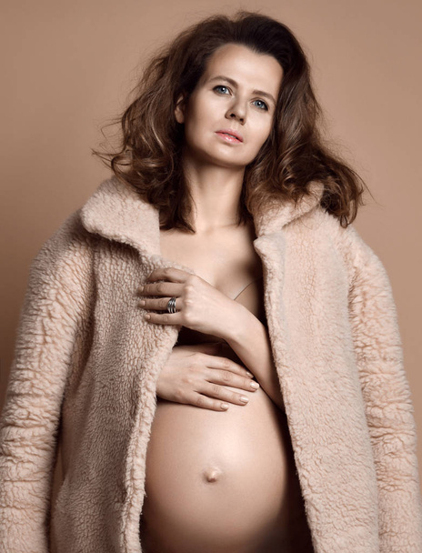 Beautiful young pregnant happy mother woman in fashion fur coat on beige  - Foto, imagen