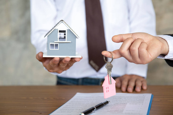 Agente imobiliário segurando modelo de casa e chaves, sinalização do cliente
 - Foto, Imagem