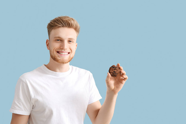 Handsome young man with tasty cookie on color background - Photo, Image