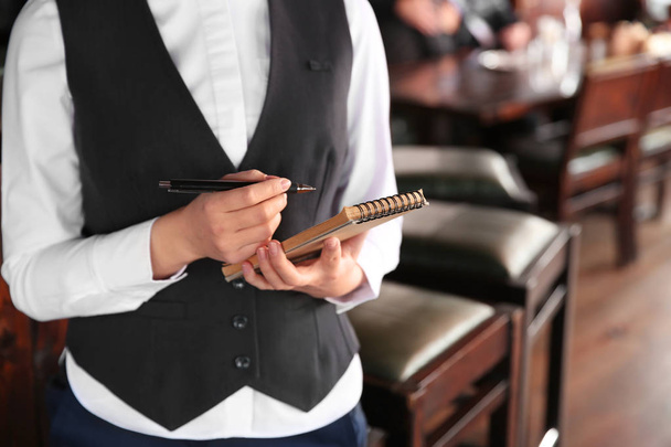 Young female waiter with notebook in restaurant, closeup - Zdjęcie, obraz