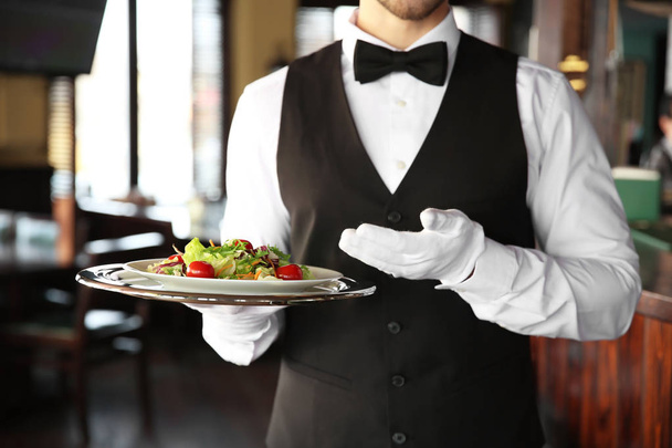 Jonge mannelijke ober met salade in restaurant - Foto, afbeelding