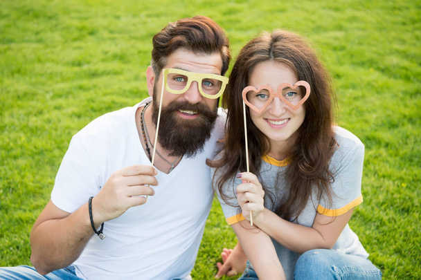 Man bearded hipster and pretty woman in love. Summer vacation. Happy together. Couple in love cheerful youth booth props. Emotional couple radiating happiness. Love story. Couple relaxing green lawn - Photo, Image