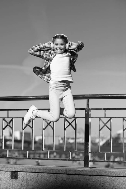 Like a rock star. Little girl jumping to music. Small happy child listening to music. Little child enjoying music playing in headphones. Cute music fan wearing wireless headset - Photo, Image