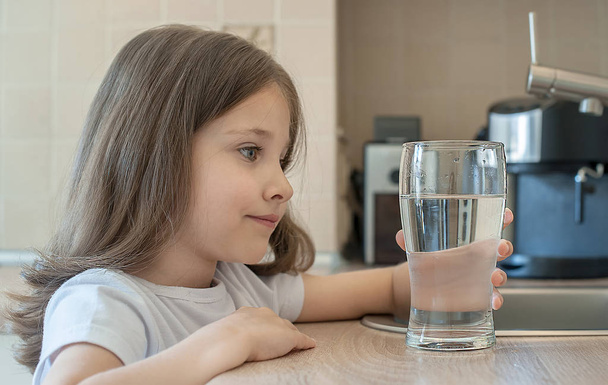 Little child is drinking clean water at home, close up. Caucasian cute girl with long hair is holding a water glass in her hands. Taking care of own health. Concept of healthy lifestyle, good habit - Fotó, kép