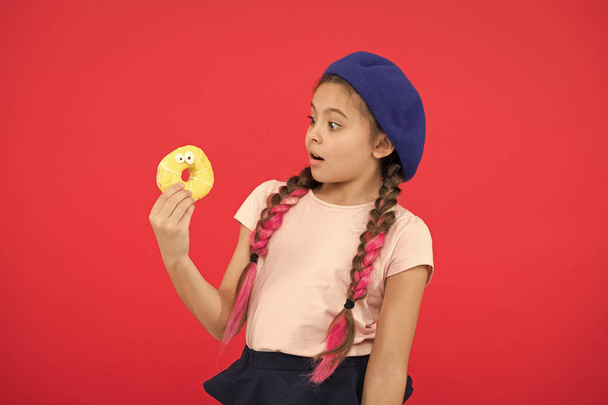 Girl in beret hat hold donut red background. Kid playful girl eat donut. Health and nutrition concept. Sweet life. Sweets shop and bakery concept. Kid fan of baked donuts. Delicious sweet donut - Fotoğraf, Görsel