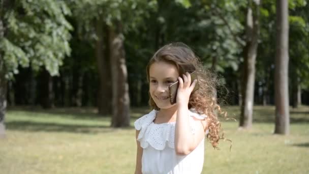 Portrait of pretty little child girl talking on mobile phone in the urban park summer day - Filmati, video