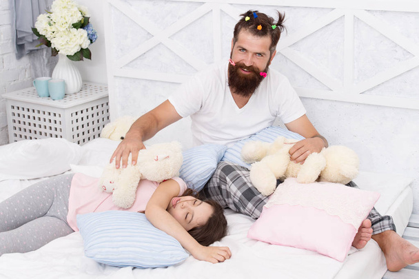 Ending of crazy evening. Having fun pajamas party. Slumber party. Happy fatherhood. Dad and girl relaxing bedroom. Pajamas style. Father bearded man funny hairstyle ponytails and daughter in pajamas - Foto, Imagen