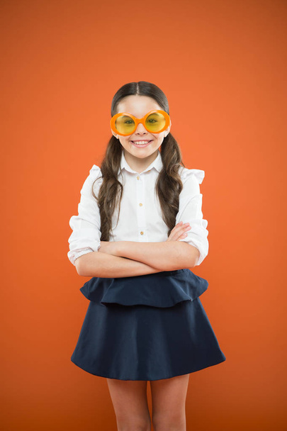 Accessory far too stylish to take off. Small kid smiling in fancy accessory on orange background. Happy girl wearing eye accessory with color filter. Little child with party look in fashion accessory - Photo, image