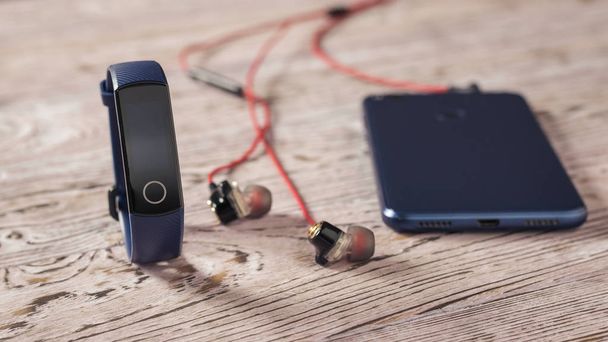 Pulsera inteligente, auriculares y smartphone en una mesa de madera tonificada. Estilo deportivo
. - Foto, Imagen