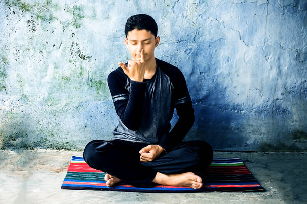 Portret strzał młodego człowieka robi Pranajama lub pranayam lub jogi kontroli oddechu na kolorowym mat z ubrany czarny strój. - Zdjęcie, obraz