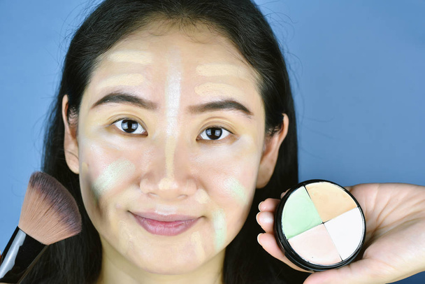 Asian kobieta stosowanie kosmetyki makijaż Fundacji i za pomocą korektor kolorów korektor, nauka robi własny makijaż. - Zdjęcie, obraz
