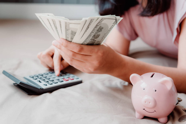 Close-Up of Beautiful Woman está calculando el ahorro de dinero mientras está acostada en su dormitorio. Concepto financiero y de inversión empresarial
.  - Foto, Imagen