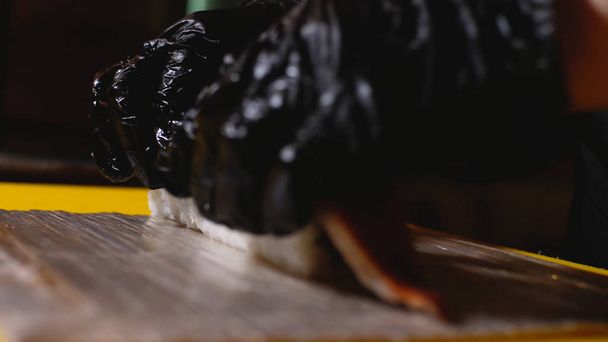 Nahaufnahme des Küchenchefs bei der Zubereitung von Sushi-Rollen mit Fisch. Rahmen. Profi-Koch in Handschuhen legt Aalstück auf Sushi-Rollen. Herstellung von ästhetischen und köstlichen Sushi-Rollen - Foto, Bild