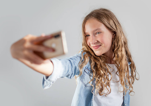 Gülümseyen genç beyaz arka plan sevimli kız üzerinde akıllı telefonda selfie fotoğraf yapma - Fotoğraf, Görsel