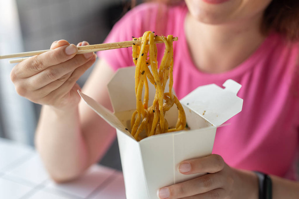 Nahaufnahme der Hand eines jungen, unbekannten Mädchens, das in einem Café Udon-Nudeln mit Holzstäbchen isst. Konzept der asiatischen Küche. - Foto, Bild