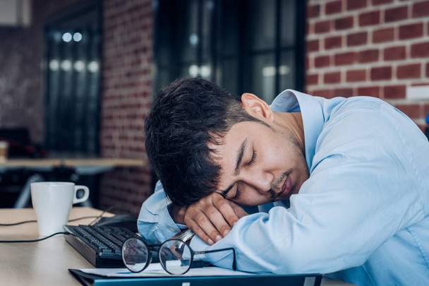 疲れたアジアのビジネスマンは、オフィスのワーキングデスクテーブルで眠ります。 - 写真・画像