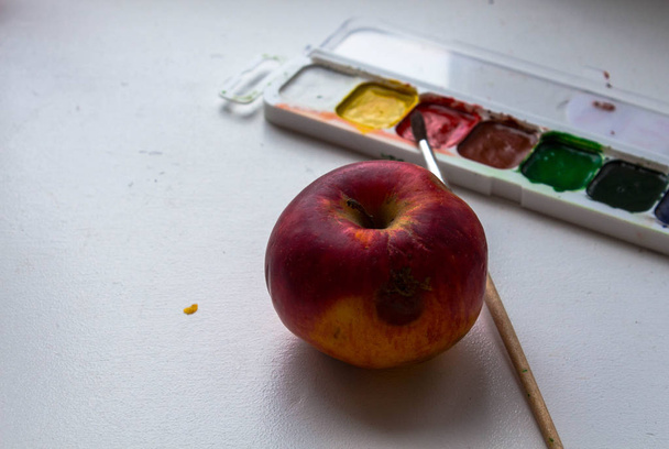 a red apple and watercolor paint and brush on white background - Photo, Image